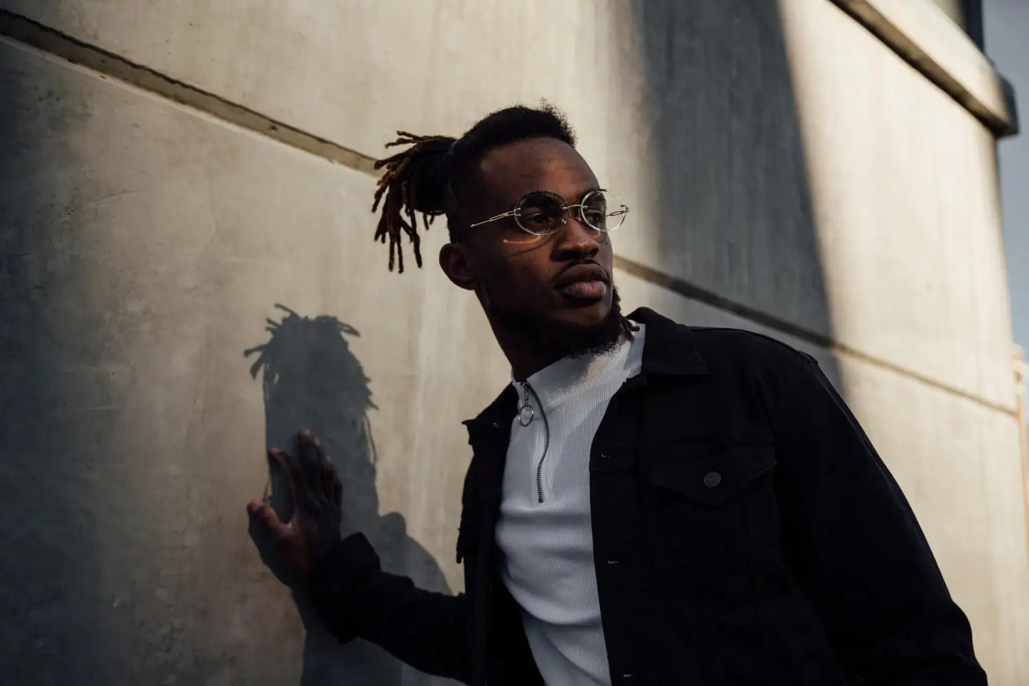 A gentleman wearing a black and white outfit leaning against a wall